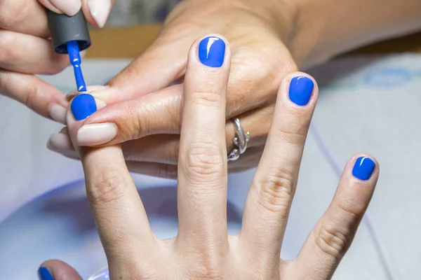 Hermoso proceso de manicura. El esmalte de uñas que se aplica a la mano, el esmalte es de color azul. de cerca — Foto de Stock