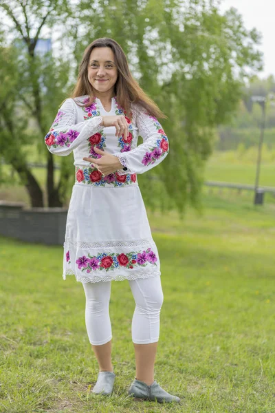 Happy young woman in the Ukrainian national clothes in the park. Woman in embroidery. Vertical photo Royalty Free Stock Photos
