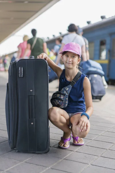 Mała słodka dziewczyna z dużą walizką na opuszczonej platformie kolejowej. Dziewczyna ciągnąc dużą walizkę na platformie. Zdjęcie pionowe — Zdjęcie stockowe