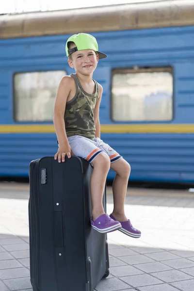 Маленький мальчик сидит на большом черном чемодане в участке. Концепция путешествия и приключений. вертикальное фото — стоковое фото