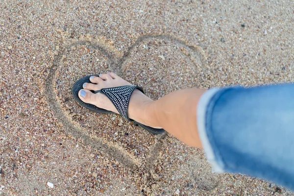 The concept of loveless love and a broken heart. Female foot crushes a heart made of sand