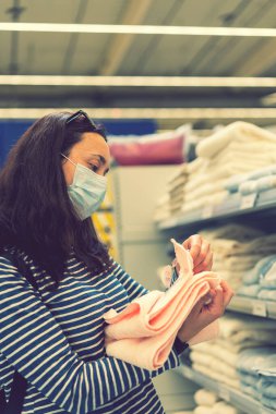 Tıbbi maskeli bir kadın mağazadan mal seçiyor. Covid-19 salgınında karantina sırasında alışveriş kavramı. Koronavirüs zamanında alışveriş. Grip maskeli güzel genç kadınlar. ses tonlu.