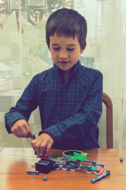 Elektrikli bir inşaatçıyı oynayan çocuk. Çocuk entellektüel oyuncaklar tarafından oynanır. Mavi gömlekli bir çocuk elektronik ustası. Çocukların erken gelişimi kavramı. Dikey fotoğraf. ses tonlu
