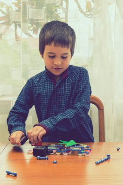 Elektrikli bir inşaatçıyı oynayan çocuk. Çocuk entellektüel oyuncaklar tarafından oynanır. Mavi gömlekli bir çocuk elektronik ustası. Çocukların erken gelişimi kavramı. Dikey fotoğraf. ses tonlu