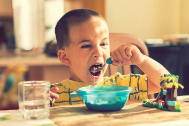 Çocuk 4 yıldır yulaf lapası yiyor. Çocuk masası. Çocuğun bağımsızlığı kavramı. Çocuk, mutfak arka planında iştahla kahvaltı yapıyor. ses tonlu.