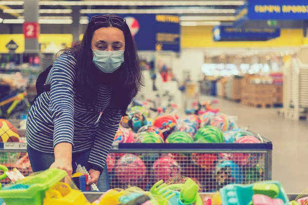 Süpermarkette koruyucu maskeli bir kadın çocuk oyuncakları seçiyor. ses tonlu.