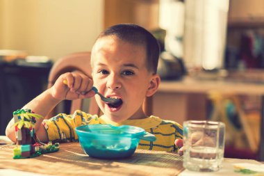 Çocuk 4 yıldır yulaf lapası yiyor. Çocuk masası. Çocuğun bağımsızlığı kavramı. Çocuk, mutfak arka planında iştahla kahvaltı yapıyor. ses tonlu.