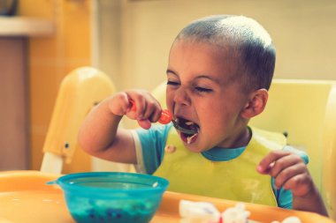 Çocuk 2 yıldır yulaf lapası yiyor. Çocuk masası. Çocuğun bağımsızlığı kavramı. Bebek koltuğundaki komik çocuk. ses tonlu.