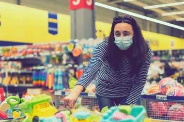 Süpermarkette koruyucu maskeli bir kadın çocuk oyuncakları seçiyor. Süpermarkette maskeli bir kadın vardı..
