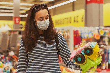 Süpermarkette koruyucu maskeli bir kadın çocuk oyuncakları seçiyor. Süpermarkette maskeli bir kadın vardı..