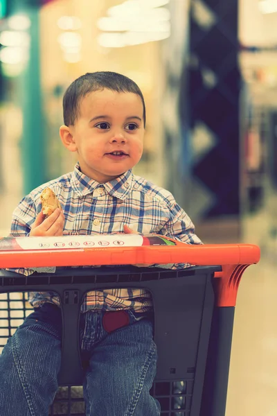Счастливый Ребенок Рубашке Сидит Тележке Торговом Центре Ест Хлеб Тонированные — стоковое фото