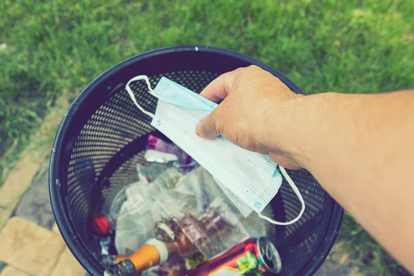 Man throwing face masks into trash in park. Man throwing used surgical mask into recycling bin. Waste disposal problem in coronavirus times, covid-19. Medical face masks. toned.