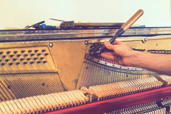 Piano tuning process. closeup of hand and tools of tuner working on grand piano. Detailed view of Upright Piano during a tuning.