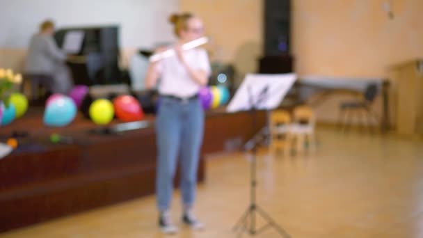 Utsikt över flickan som spelar på flöjt. Tonårstjejen spelar flöjt i konsertsalen. dimmigt — Stockvideo