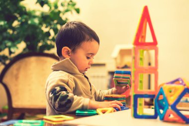 Çocuk 2 yıldır parlak bir inşaatçıdan kule inşa ediyor. Küçük gülümseyen çocuk manyetik oyuncaklarla oynuyor. Entellektüel oyuncaklar oynayan bir çocuk. Mor tonlama. ses tonlu.