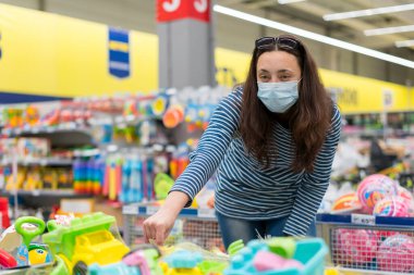 Süpermarkette koruyucu maskeli bir kadın çocuk oyuncakları seçiyor. ses tonlu.