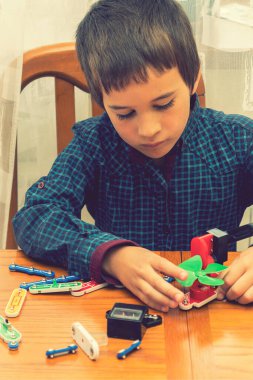 Elektrikli bir inşaatçıyı oynayan çocuk. Çocuk entellektüel oyuncaklar tarafından oynanır. Mavi gömlekli bir çocuk elektronik ustası. Çocukların erken gelişimi kavramı. Dikey fotoğraf. ses tonlu.