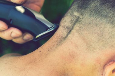 Eller elektrikli saç makasıyla çocuğun uzun saçını keser, berber dükkanında berber olur, aileler kuaförler kapalıyken saç keser, evde kalıp konsept yapar. Gülümseyen çocuk. ses tonlu.