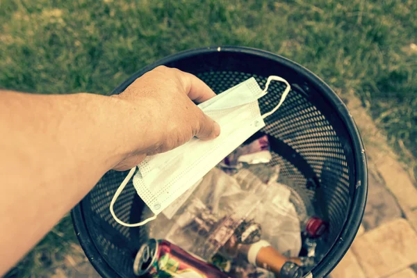 Man throwing face masks into trash in park. Man throwing used surgical mask into recycling bin. Waste disposal problem in coronavirus times, covid-19. Medical face masks. toned.