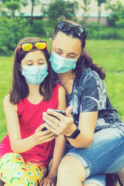 Mom with daughter in the park in medical masks. Family of mom and kid wearing protective medical mask for prevent virus outdoors in the park. new normal concept. toned.