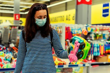 Süpermarkette koruyucu maskeli bir kadın çocuk oyuncakları seçiyor. ses tonlu
