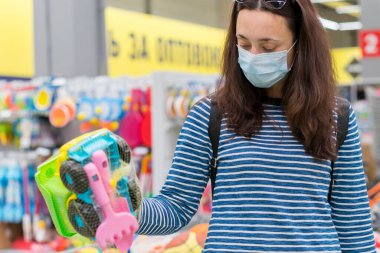 Süpermarkette koruyucu maskeli bir kadın çocuk oyuncakları seçiyor. Süpermarketteki tıbbi maskeli kadın..