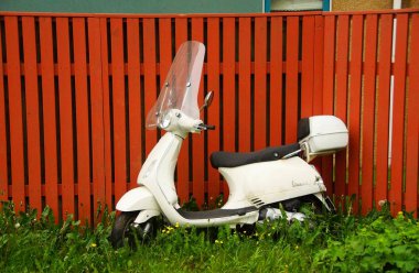 Kahverengi bir çitte beyaz bir Vespa scooter.