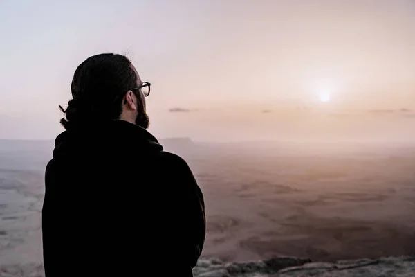 Solo el hombre en el desierto de Israel Néguev admira la vista del amanecer. Joven hombre se encuentra en el borde del acantilado — Foto de Stock