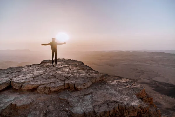 Solo el hombre en el desierto de Israel Néguev admira la vista del amanecer. Joven hombre se encuentra en el borde del acantilado — Foto de Stock