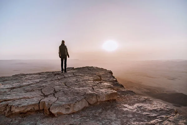 Solo el hombre en el desierto de Israel Néguev admira la vista del amanecer. Joven hombre se encuentra en el borde del acantilado — Foto de Stock