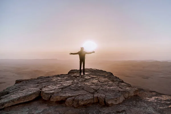 Solo el hombre en el desierto de Israel Néguev admira la vista del amanecer. Joven hombre se encuentra en el borde del acantilado — Foto de Stock