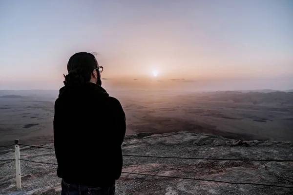 Solo el hombre en el desierto de Israel Néguev admira la vista del amanecer. Joven hombre se encuentra en el borde del acantilado — Foto de Stock