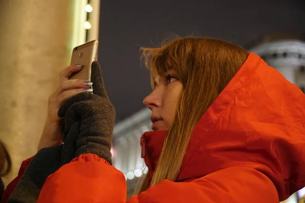 Avrupa Noel piyasasında Smartphone kullanan kadın. Kız zevk kış tatil sezonu, kullanılması telefon, sosyal ağ bulanık Noel ışıkları arka planda, alacakaranlıkta.