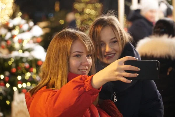 Avrupa Noel piyasasında Smartphone kullanan kadın. Kız zevk kış tatil sezonu, kullanılması telefon, sosyal ağ bulanık Noel ışıkları arka planda, alacakaranlıkta.