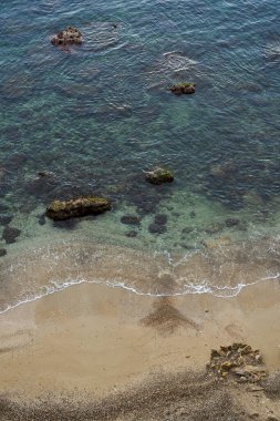 Şeffaf deniz suyu, kayalar ve yumuşak dalgalar kumsala ulaşıyor.