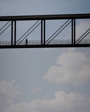 Bir köprü bir bulutlu gökyüzü karşı yürüyen bir kadın silüeti