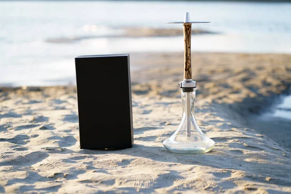 Güneş ışınları nehir kıyısında parlak kum üzerinde bir kara kutu ile temiz şeffaf bir kase ile bir elektrik akımı yıldırım desenleri ile Bej ahşap nargile.