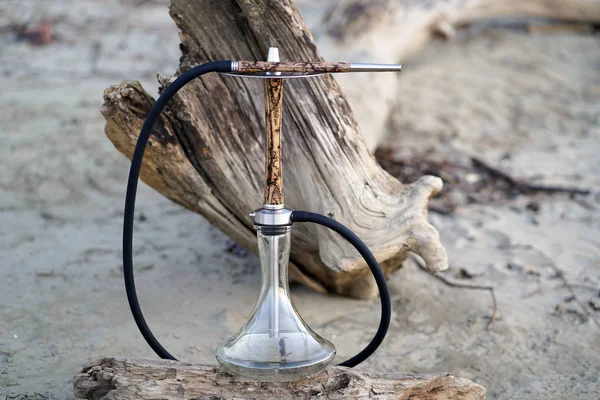 Düşmüş bir ağacın arka planına karşı ormanda bir günlük üzerinde metal elemanları ile bir hortum ile temiz bir şeffaf kase ile bir elektrik akımı yıldırım desenleri ile Bej ahşap nargile.