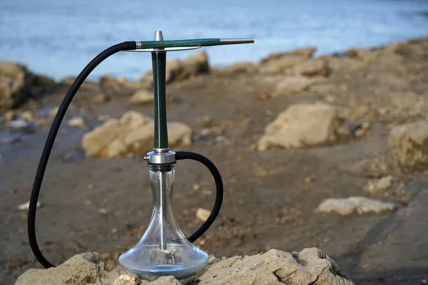 Siyah hortumlu mavi ahşap nargile bir taş üzerinde deniz üzerinde duruyor. Metal bir plaka nın üzerinde ağızlık. Seyahat ve sigara nargile için kavram. Doğanın bulanık arka planı ve mavi su.