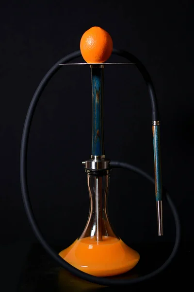 Siyah bir arka plan üzerinde koyu bir hortum ile metal plaka turuncu ile Modern mavi ahşap nargile. Bir kavanoz suda portakal suyu.
