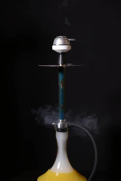 Siyah bir arka plan üzerinde su kavanozunda kömürler ve sarı suyu ile Lüks mavi ahşap nargile. Serbest bırakma vanasından bir duman bulutu.