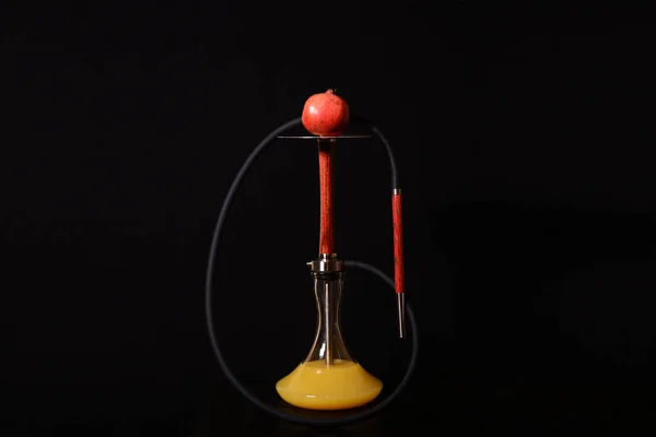 Koyu bir arka plan üzerinde metal elemanları ile bir nar meyve ve siyah hortum ile Modern kırmızı ahşap narnar. Su kavanozundaki sarı meyve suyu.