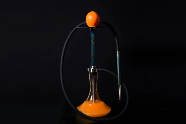 Siyah bir arka plan üzerinde koyu bir hortum ile metal plaka turuncu ile Modern mavi ahşap nargile. Bir kavanoz suda portakal suyu.