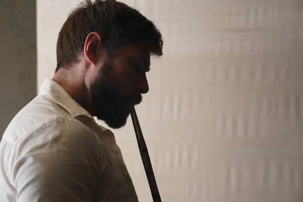 Beyaz bulanık arka plan üzerinde beyaz buruşturulmuş gömlek kısa kahverengi saçlı acımasız sakallı bir adamın profilinde Portre. Yakışıklı erkek nargile içer ve ahşap bir ağızlık ile duman teneffüs.