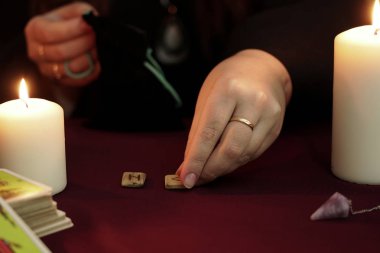 Cadı siyah mantolu bir falcı. Masasında antik mühürler var. Tarot kartları, ametist taşları, karanlık ve gizemli arka planda beyaz mumlar. Okült, esrarengiz, kehanet ve cadı kavramı.