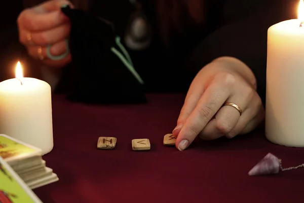 Cadı, elinde yüzük olan siyah mantolu bir falcı. Masaya antik mühürler koyuyor. Tarot kartları, ametist taşları, karanlık ve gizemli arka planda beyaz mumlar. Okült, esrarengiz, kehanet ve cadı kavramı.