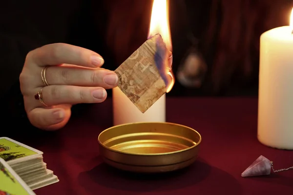 Cadı, siyah mantolu bir falcı sihirli bir ayin yapıyor ve elinde yanan kağıtlar tutuyor. Tarot kartları, ametist taşı, arka planda beyaz mumlar. Okült, esrarengiz, kehanet ve cadı kavramı