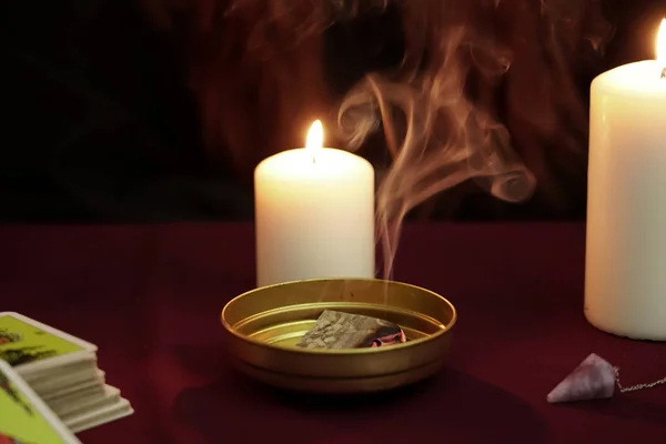 Magiske ritualer med ulmende papir med røyk i gylden bolle. Tarotkort, ametyststein, hvite lys på mørk, mystisk bakgrunn. Okkulte, esoteriske, spådommer og wicca-konseptet . – stockfoto