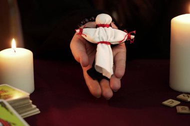 Bornozlu cadı kırmızı iplikle bağlanmış siyah ve beyaz oyuncak bebeklere tutunuyor. Üstte beyaz. Tarot kartları, eski mühürler ve beyaz mumlar. Esrarengiz, esrarengiz, kehanet ve cadı kavramı. Gizemli arkaplan.