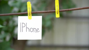 Bulanık arka planda sarı clothespin üzerinde beyaz etiket üzerinde Yazıt. Boş pim yakınında metal bir çubuk üzerinde solda asılı kelime Iphone ile alone kağıt. 